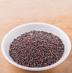 Black mustard seed in white bowl on wooden surface