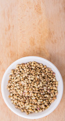 Coriander seeds in white bowl on wooden surface