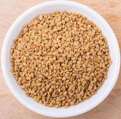 Fenugreek seeds in white bowl on wooden surface