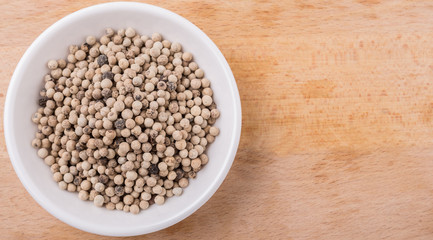 White pepper in white bowl on wooden surface