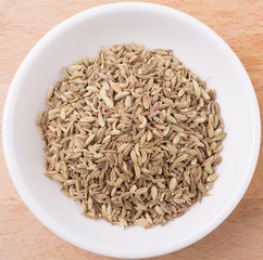 Cumin seed spice in white bowl on wooden surface