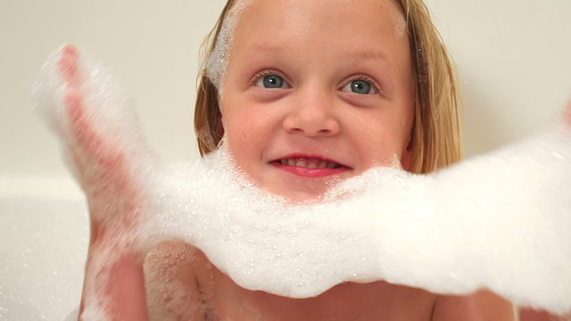 A baby and a little girl make a beard out of suds while sitting in a bubble bath