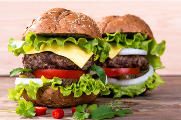 Big hamburger with beef cutlet and vegetables on wood background