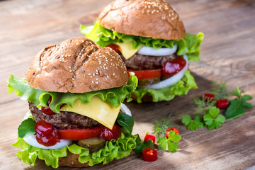 Big hamburger with beef cutlet and vegetables on wood background