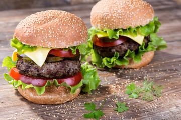 Big hamburger with beef cutlet and vegetables on wood background