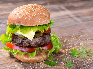 Big hamburger with beef cutlet and vegetables on wood background