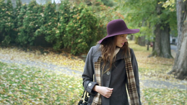 A young woman looks into the camera and then begins to walk away down the sidewalk