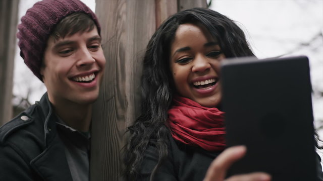 A couple laugh together as they try to take a picture with their tablet