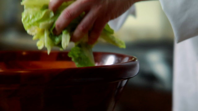 a chef picking salad from a bowl and placing it on a plate