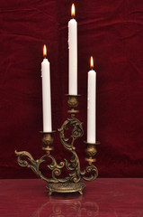 Antique candelabra with three melting candles on a dark red velv