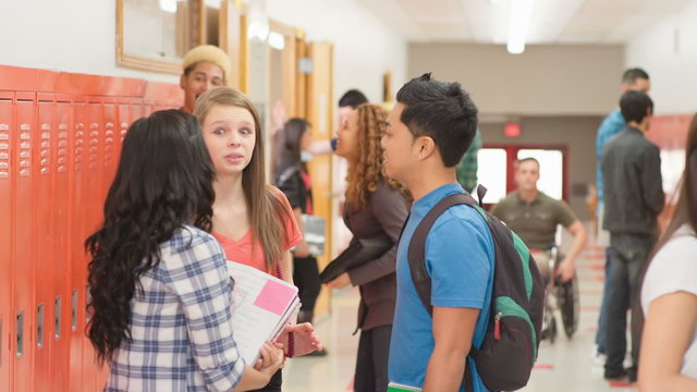 A high school hallway scene with students and a teacher