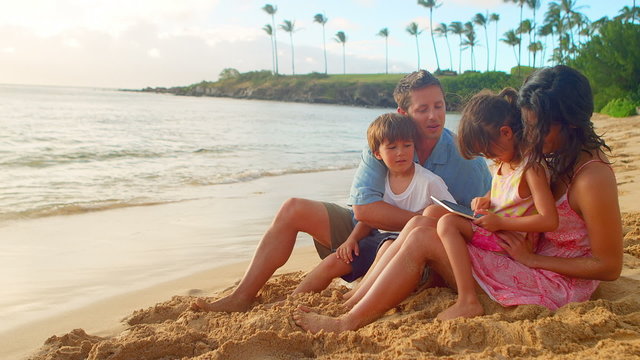 A family sits on the beach and look through a tablet