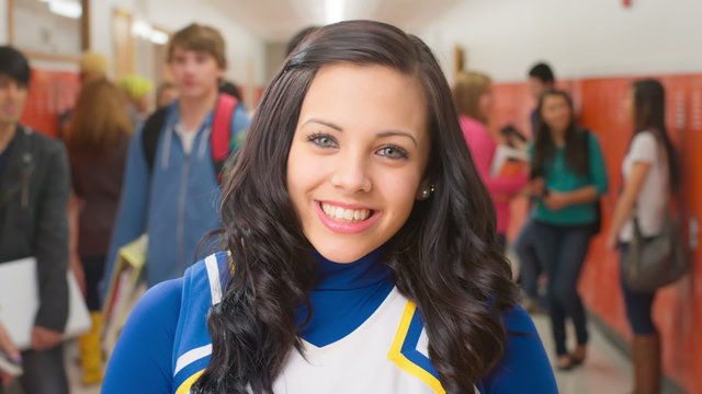 A female student dressed as a cheerleader stands in a hallway with other kids