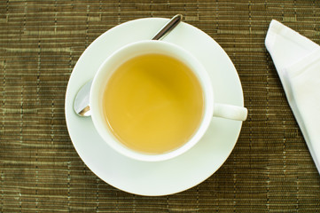 Cup of yellow tea in white tableware on bamboo napkin top view