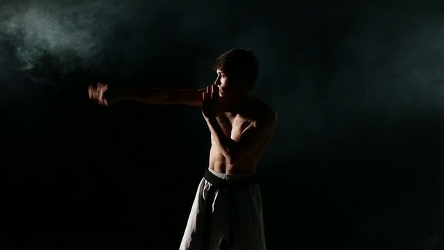 Karate or taekwondo training man punches smoke, close up. white