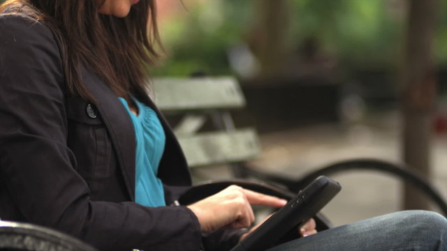 A young woman is sitting on a bench using a tablet computer
