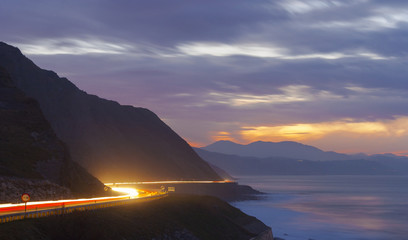 Car lights in the road at night, by the sea © poliki