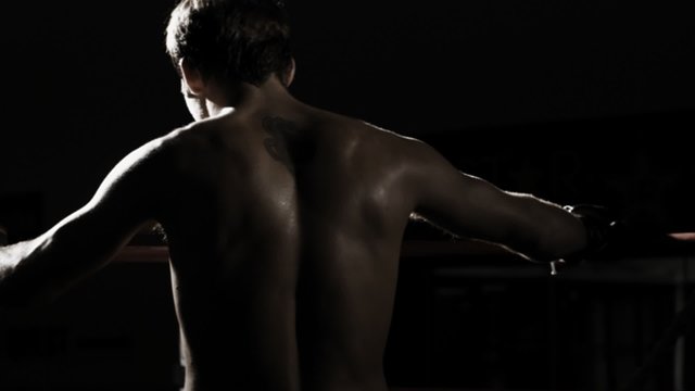 A boxer stands in the corner of the ring and prepares to fight in the shadows