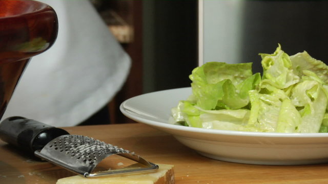 Close up of a chef putting salad on a plate and then grating cheese over it