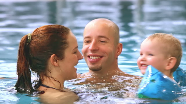 A father and mother swimming in the pool with their son the kiss