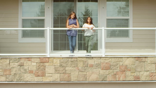 Two young sisters stand on the balcony of their house, in slow motion