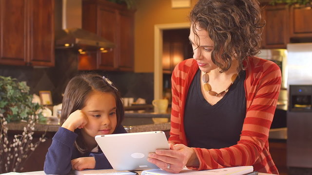 A mom uses a digital tablet to home school her little girl