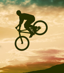 Silhouette of a man doing a jump with a bmx bike against sunset