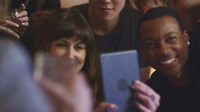A group of friends at a party use a tablet to take pictures of themselves