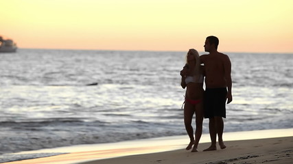 A cute couple take a stroll on a beach in Mexico during a sunset