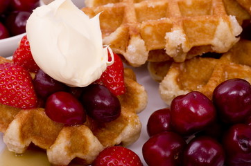 A pile of Belgian Waffles, fresh summer fruits with maple syrup