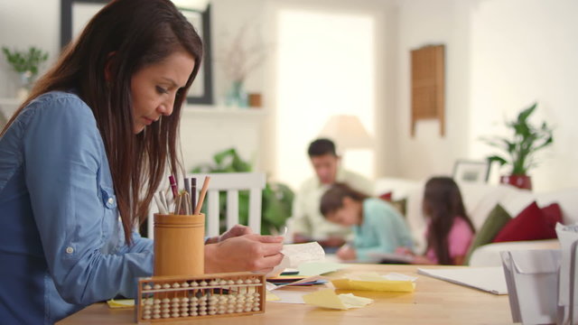 A mother goes over bills and looks worried as her family sits behind her