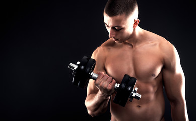 Fototapeta na wymiar Young man with bare chest lifting dumbbells on black background.