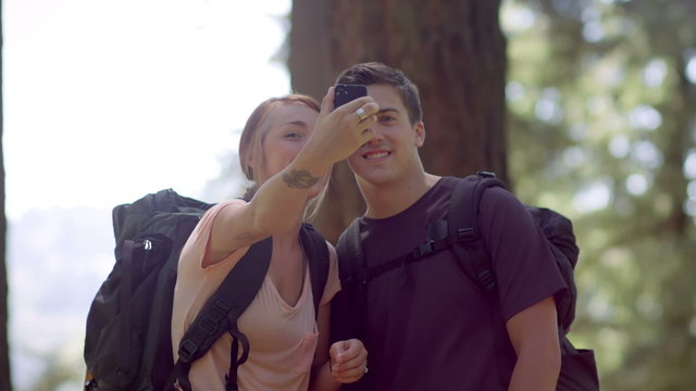 Fit and healthy young couple hikes through park and stops to take photo