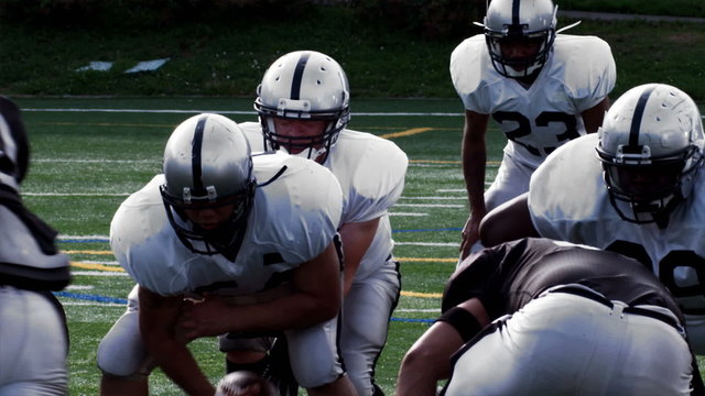 A Quarterback hikes the ball and avoids rushers before passing the ball.