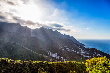 Mountains with clouds and sun over small village