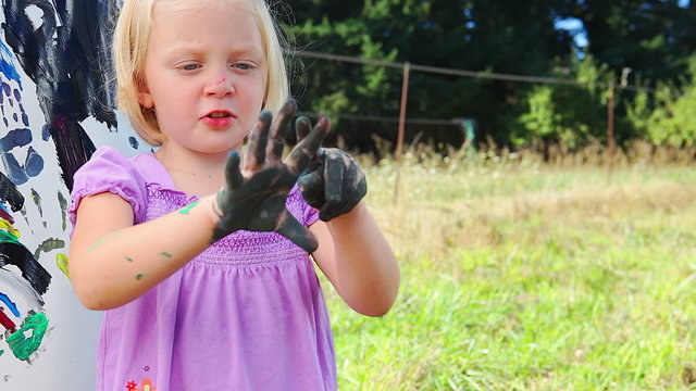 A young girl counts her fingers while her hands are covered in paint