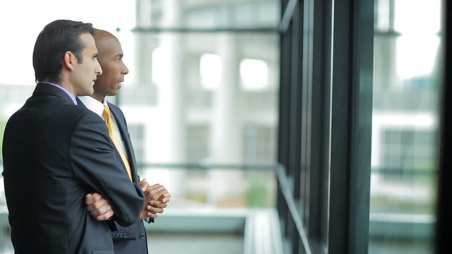 Two male Business Professionals Work Together, while looking out a window