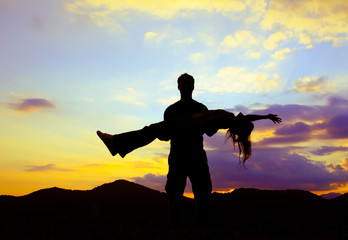 Fototapeta na wymiar silhouette of man lift woman up on mountain at sunset