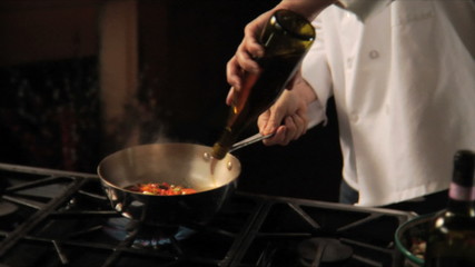 A chef sautéing vegetables and sausage in a pan in a kitchen, with flames