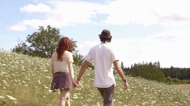 Wide shot of couple in field holding hands walking away from the camera