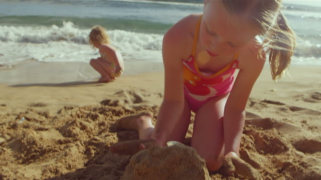 Two young girls build a sandcastle while playing at the beach