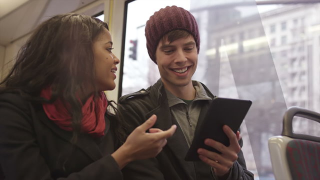 A young couple ride the tram and look at a tablet together and laugh