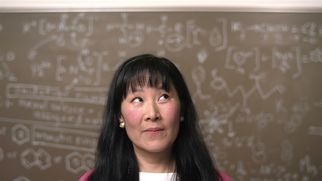 A female Asian college student stand in front of a chalkboard with equations 