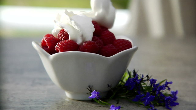 Whipped cream being put on top of a bowl of raspberries