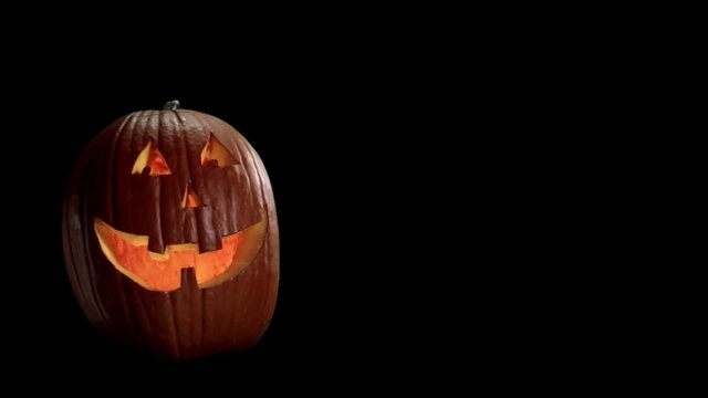 A Jack-o-lantern with a smiling face flickers on a black background