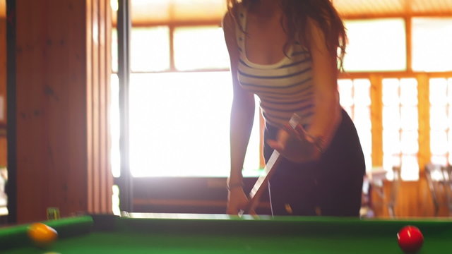 A young woman hitting the cue ball on a green billiard table