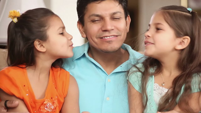 A father holds and kisses his two young daughters