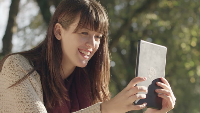 A young woman in the park uses her tablet to take pictures and selfies