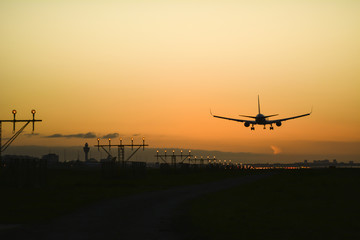 Naklejka na ściany i meble Airplane landing with an orange sky at the background.