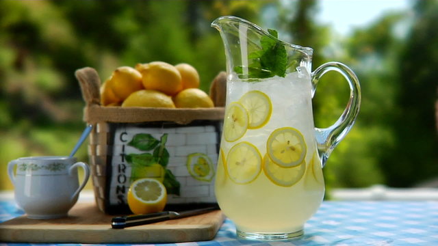 pitcher of lemonade and glasses getting picked on a table outside 